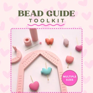 Puede incluir: Un kit de guía para cuentas que incluye una herramienta de medición rosa claro en forma de arco con el texto SYLMOUETTE STUDIOS, acompañado de varias cuentas coloridas con formas de corazones, mariposa y pájaro, montadas en alfileres metálicos dorados.