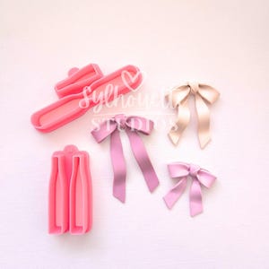May include: Pink bow-shaped cookie cutters and finished bows in various shades of pink and beige. The image includes two cookie cutter designs and three finished bows, perfect for baking and decorating. The text "Silhouette Studios" is visible.