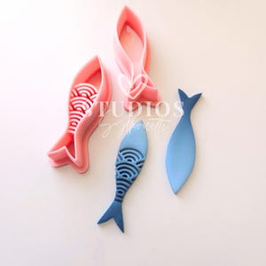 May include: Three fish-shaped cookie cutters, two pink and one blue. The pink cutters have a detailed design of scales and the blue cutter is solid.
