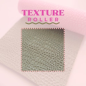 以下が含まれることがあります： テクスチャローラーのピンクと白の画像。「TEXTURE ROLLER」の文字はピンク色で、緑色の波線の上にあります。テクスチャ加工された素材の正方形が強調表示され、ワニの皮に似たパターンが示されています。