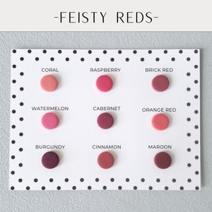 May include: A white card with black polka dots displays nine circular color samples in shades of red. The colors are labeled: Coral, Raspberry, Brick Red, Watermelon, Cabernet, Orange Red, Burgundy, Cinnamon, and Maroon. The text "-FEISTY REDS-" is at the top.