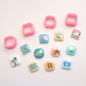 May include: Three pink plastic square cookie cutters and eleven small square tiles with various colorful illustrations including palm trees, a crab, a mango, pasta, olives, and floral patterns, featuring the text Sylhouette Studios.