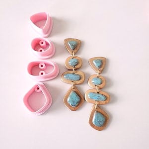 以下が含まれることがあります： ターコイズストーンが付いた長いゴールドトーンのイヤリングのペア。イヤリングはポリマークレイ製で、幾何学的なデザインです。イヤリングは、ピンクのシリコンモールド4つと一緒に表示されています。