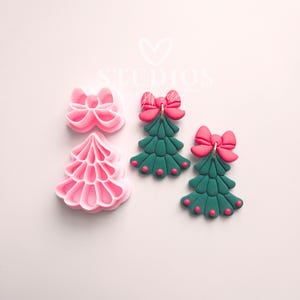 May include: Pink and green Christmas tree-shaped earrings and cookie cutters. The earrings have a green tree design with a red bow and red dot accents. The cookie cutters are pink, one shaped like a bow and the other like a Christmas tree.