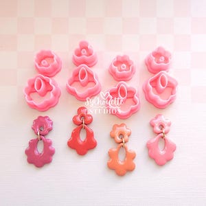 May include: A collection of pink flower-shaped polymer clay earring cutters and finished earrings. The earrings are in shades of pink and orange, with gold-colored hardware. The image includes the text "Silhouette Studios".