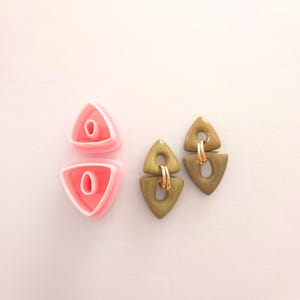 May include: Two pairs of earrings, one pair is pink and the other is green. The pink earrings are triangle shaped and the green earrings are triangle shaped with a gold accent.