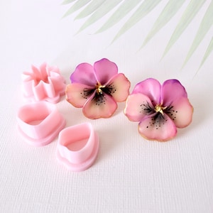 Puede incluir: Un juego de cortadores de flores de plástico rosa para hacer flores de fondant o pasta de goma. El juego incluye dos cortadores en forma de corazón, un cortador en forma de estrella y dos cortadores en forma de pensamiento.