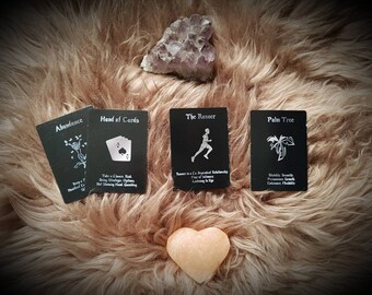 May include: Four black cards with white illustrations and text on a brown fuzzy surface. The cards are titled "Abundance", "Hand of Cards", "The Runner", and "Palm Tree".