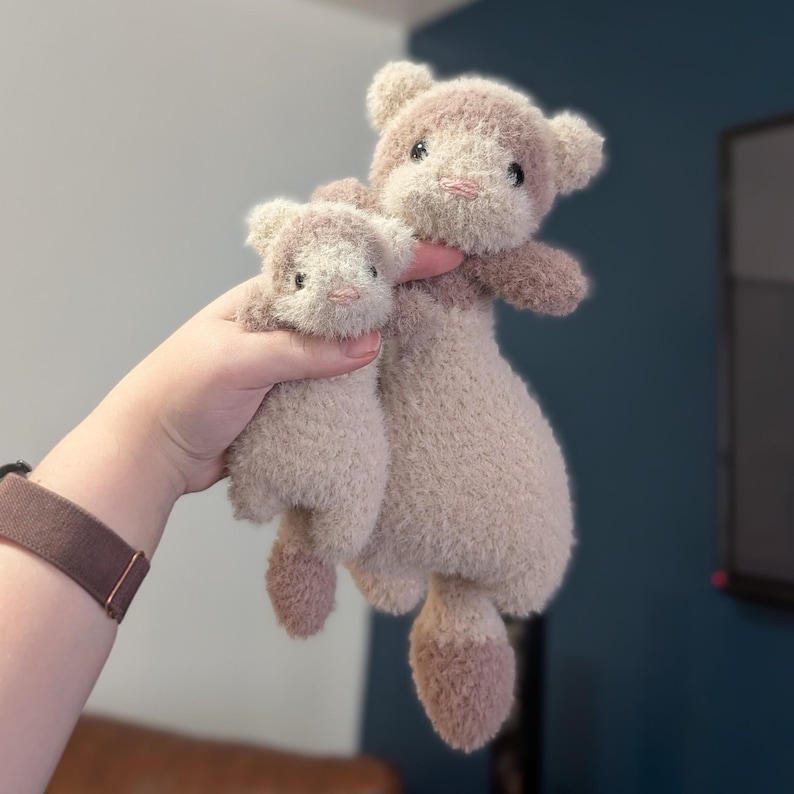 Op de afbeelding: Twee pluche teddyberen in beige en bruine tinten. De grotere beer houdt de kleinere vast. De beren hebben kleine zwarte ogen en roze neuzen. De zachte, donzige vacht suggereert een knuffelig speelgoed.