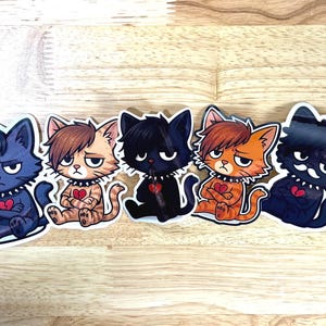May include: Five stickers featuring cartoon cats with emo hairstyles, each with a broken heart and studded collar. The cats are in various colors: blue, brown, black, orange, and dark blue. They are sitting with arms crossed.