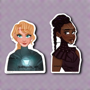 May include: Two stickers featuring stylized illustrations of female characters. One has blonde hair and teal eyes, wearing a dark suit with a glowing chest piece. The other has dark hair, braids, and face paint, wearing a dark purple outfit.