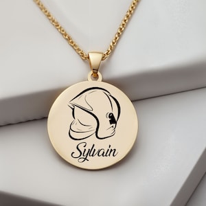 Peut inclure: Collier en or avec un pendentif rond représentant une silhouette noire de casque de pompier et le nom Sylvain.