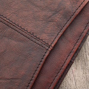 May include: Close-up of brown leather with a stitched seam. The leather has a textured surface.