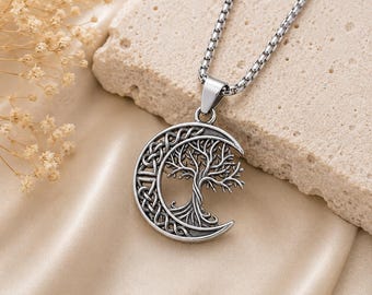 May include: A silver-toned metal pendant necklace featuring a crescent moon shape. One side of the moon displays an intricate Celtic knotwork pattern, while the other side depicts a detailed tree with branches and roots. It hangs on a box chain.
