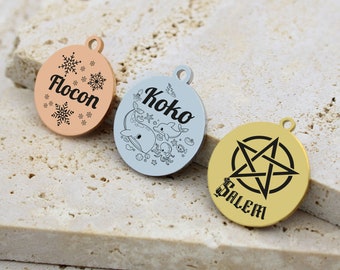 May include: Three round metal tags with different designs and names. The first tag is rose gold with snowflakes and the name "Flocon". The second tag is silver with a whale, dolphin, and other sea creatures and the name "Koko". The third tag is gold with a pentagram and the name "Salem".