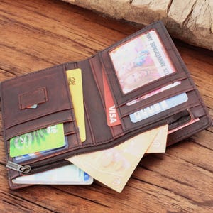 May include: A brown leather wallet with a zippered compartment, open to reveal multiple credit cards, cash, and a photo ID. The wallet has a worn, distressed look.