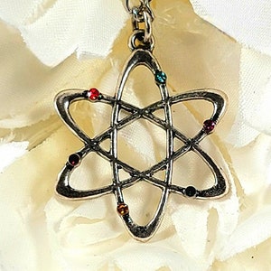 Może przedstawiać: Srebrny naszyjnik w kształcie atomu z kolorowymi kryształkami. Naszyjnik leży na białym tle.