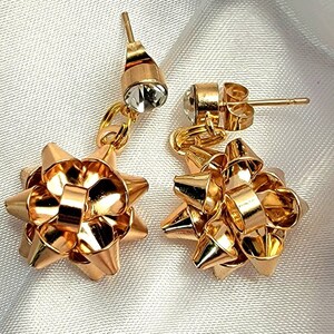 May include: Gold bow earrings with a clear rhinestone accent. The earrings are dangling and have a bow shape.