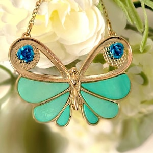 Könnte beinhalten: Eine goldene Schmetterlingskette mit türkisfarbenen Flügeln und blauen Blumenakzenten.