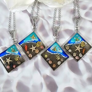 May include: Four silver necklaces with square pendants featuring a blue and white seascape with seashells and a sailboat. The pendants are filled with resin and have a glossy finish.