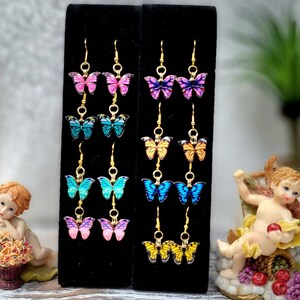 May include: A set of 10 pairs of butterfly earrings on a black display card. The earrings are gold-toned and feature colorful butterfly designs with various colors, including pink, blue, yellow, and purple.