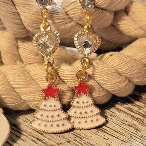 May include: A pair of gold-tone earrings with a heart-shaped crystal charm and a white Christmas tree charm with a red star on top.