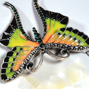 May include: A silver butterfly brooch with green and black enamel wings and clear rhinestones. The wings are decorated with a light orange and yellow pattern.