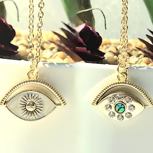 May include: Two gold necklaces with a spinning eye pendant. One eye has a white background with a sun design, the other eye has a green and blue background with clear rhinestones.