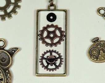 May include: A silver necklace with a rectangular pendant featuring a white background and three small, intricate gears. The pendant is surrounded by various bronze gears and clock-shaped charms.
