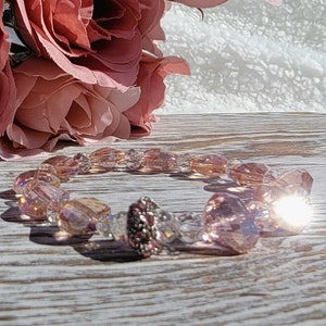 May include: A pink and white crystal bracelet with a flower design. The bracelet is made of glass beads and has a delicate, feminine look.