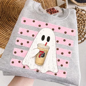 May include: A heather gray crewneck sweatshirt featuring a white ghost graphic holding a plastic cup of iced coffee with a red straw. The ghost is centered over horizontal pink brushstroke stripes with brown polka dots. A 270 Fits tag is at the neck.