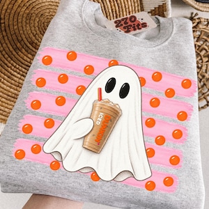 Peut inclure: Un sweat-shirt gris chiné à col rond avec un motif de fantôme blanc tenant un café glacé portant l'inscription Dunkin Iced. Le design présente des coups de pinceau roses horizontaux et des pois orange. Une étiquette indique 270 Fits au col.