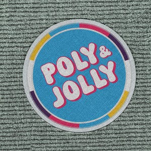 May include: A round patch with the words "POLY & JOLLY" in white, outlined in pink, on a blue background. The patch has a white border with sections of yellow, pink, and purple. The patch is on a textured gray surface.