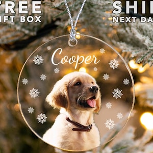 May include: A clear round Christmas ornament with a photo of a golden retriever puppy. The ornament has snowflakes and the name "Cooper" engraved on it.