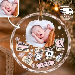 May include: A round, faceted glass ornament featuring a central photograph of a sleeping baby. The design includes pink icons of a measuring tape labeled 19 INCHES, a scale labeled 8 lb 5oz, a calendar showing 19 AUGUST, a clock, a bottle, and text reading CORDOVA ALASKA and CELIA.