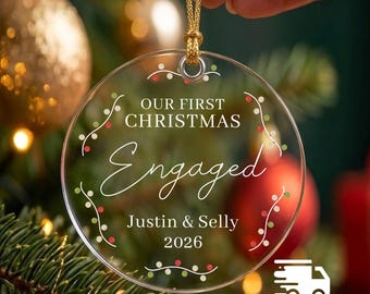 Könnte beinhalten: Ein runder, durchsichtiger Acryl-Weihnachtsanhänger mit einer goldenen Aufhängeschnur. Der Text "OUR FIRST CHRISTMAS Engaged Justin & Selly 2026" ist in Weiß gedruckt, umgeben von einer feinen, kreisförmigen Rankengrafik mit roten und grünen Punkten.