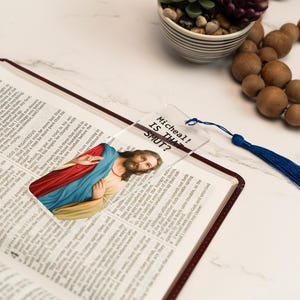 May include: A clear glass bookmark with a picture of Jesus Christ and the text "Mitcheall! Is that SHUT?" printed on it. The bookmark has a blue tassel.