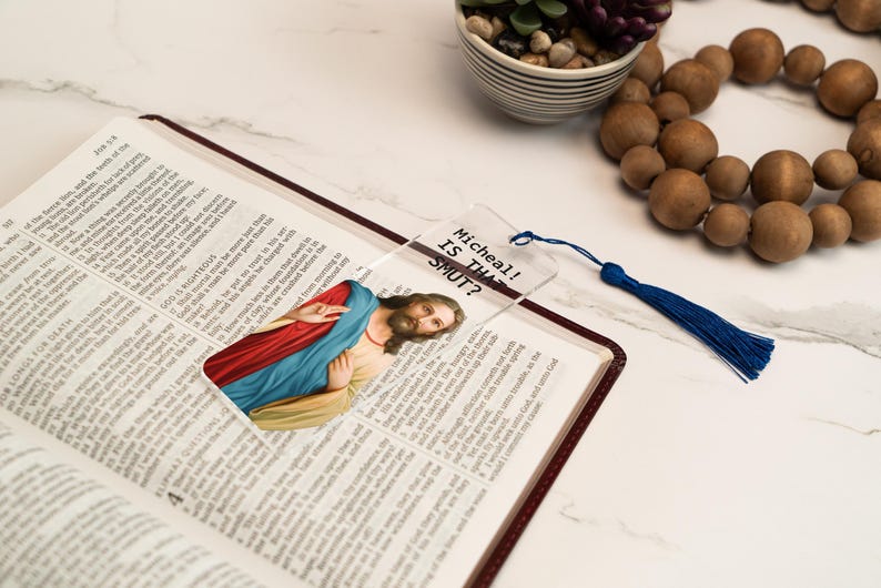 May include: A clear glass bookmark with a picture of Jesus Christ and the text "Mitcheall! Is that SHUT?" printed on it. The bookmark has a blue tassel.
