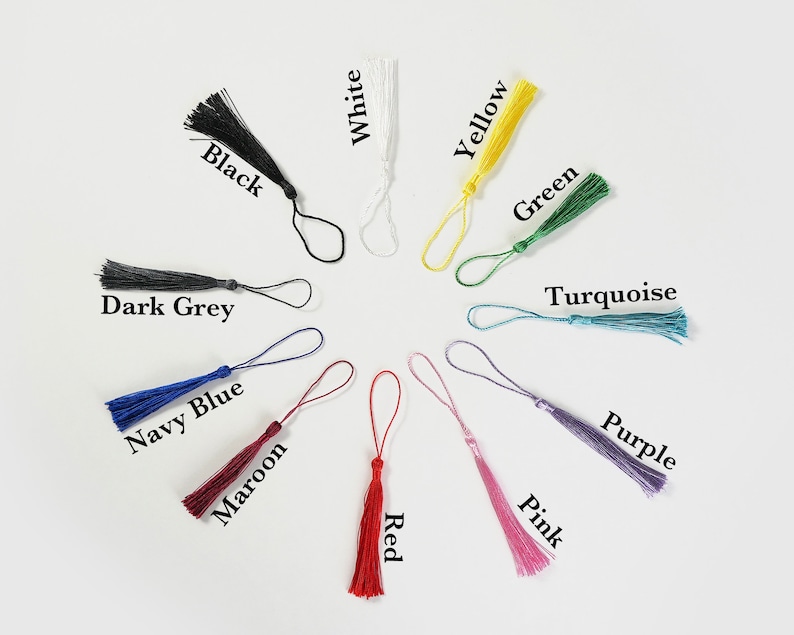 May include: Assortment of 12 tassel keychains in various colors, including black, white, yellow, green, turquoise, purple, pink, navy blue, maroon, red, and dark grey. Each tassel is attached to a small loop.