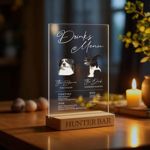 May include: A clear acrylic sign with a drinks menu for a bar called "Hunter Bar". The sign features illustrations of two dogs, one named "The Bruno" and the other named "The Feck". The menu lists cocktails, wine, beer, and spirits.