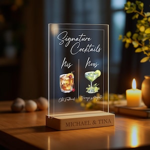 May include: A clear acrylic sign with a wooden base, displaying "Signature Cocktails" with illustrations of two cocktails, labeled "His" and "Hers". The sign is personalized with the names "MICHAEL & TINA".