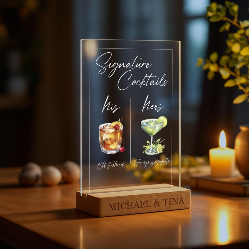 May include: A clear acrylic sign with a wooden base, displaying "Signature Cocktails" with illustrations of two cocktails, labelled "His" and "Hers". The sign is personalised with the names "MICHAEL & TINA".