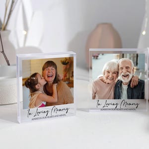 May include: Two clear acrylic photo blocks, each displaying a photograph. One shows a woman and a child, the other an elderly couple. The text "In Loving Memory, Always in our hearts and minds" is printed on each block.
