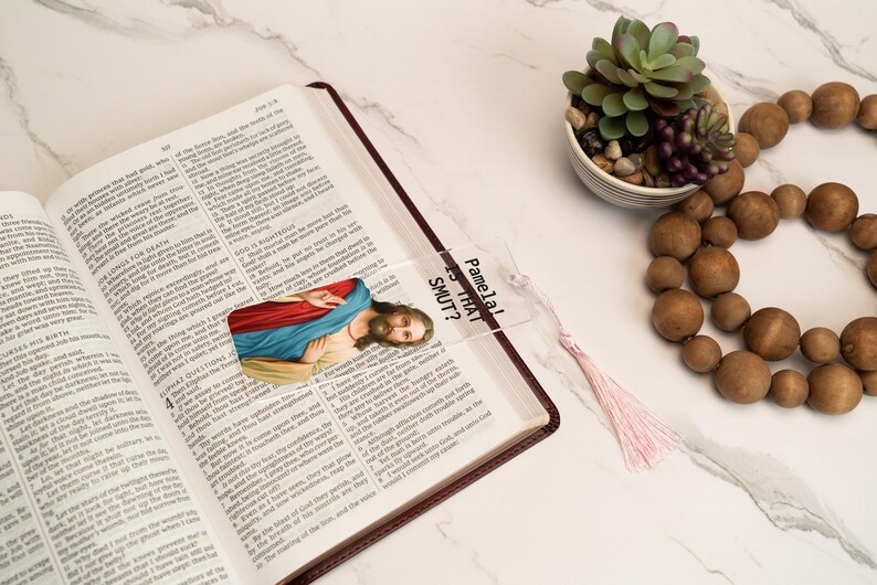 May include: A clear plastic bookmark with a picture of Jesus and the text "Pamela Is That Sh*t?" printed on it. The bookmark has a pink tassel.