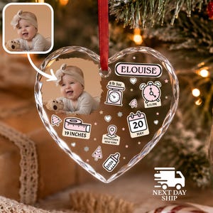K&ouml;nnte beinhalten: Ein herzf&ouml;rmiger, transparenter Acryl-Weihnachtsbaumschmuck mit einem Babyfoto, dem Namen Elouise und Geburtsdaten wie 3,77 kg, 21:11 Uhr, 48,26 cm, 20. Mai, Smithtown New York und 2026, verziert mit rosa Symbolen und einem roten Band.