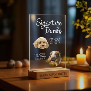 May include: A clear acrylic sign with the text "Signature Drinks" and two dog illustrations. The sign has a wooden base with the text "Mark's Favorites".