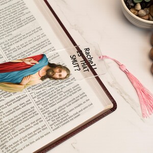 May include: A clear bookmark with a pink tassel. The bookmark features a printed image of Jesus Christ and the text "Rachel Is That Smut?"