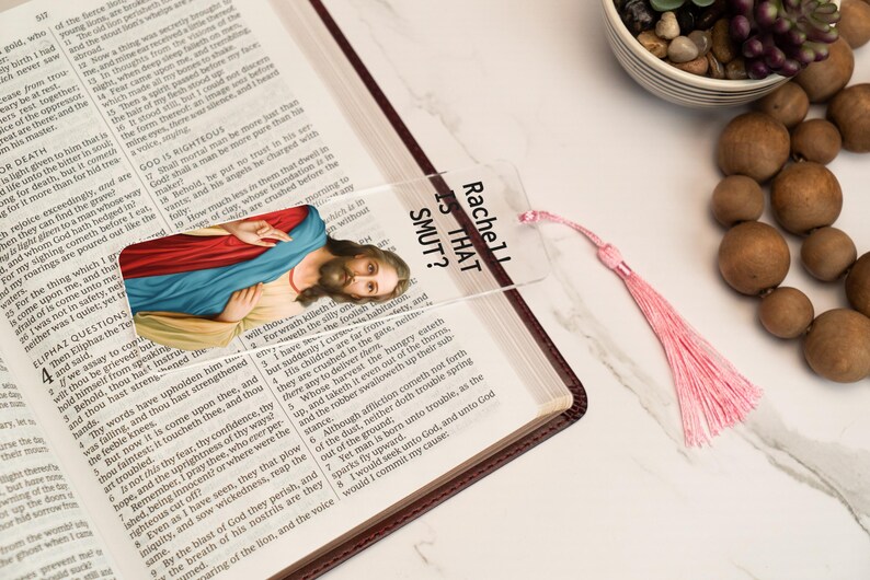 May include: A clear bookmark with a pink tassel. The bookmark features a printed image of Jesus Christ and the text "Rachel Is That Smut?"