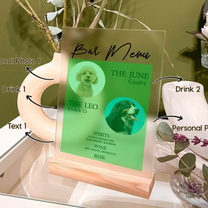 May include: A clear acrylic sign with a wooden base, featuring a bar menu with two dog photos and drink names. The menu includes "The Leo, French 75", "The June, Gimlet", and a list of spirits, wine, and beer.