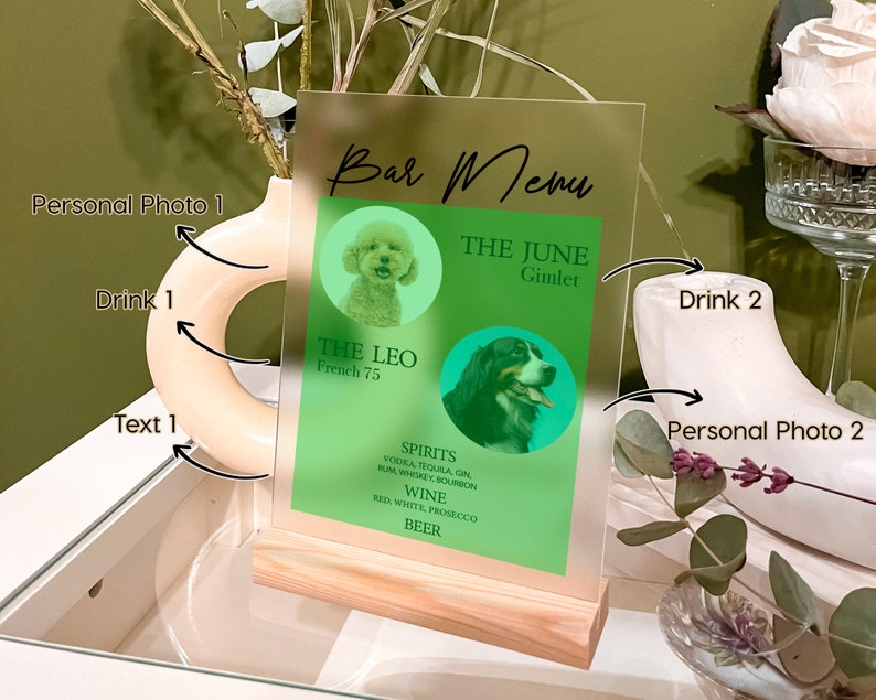 May include: A clear acrylic sign with a wooden base, featuring a bar menu with two dog photos and drink names. The menu includes "The Leo, French 75", "The June, Gimlet", and a list of spirits, wine, and beer.